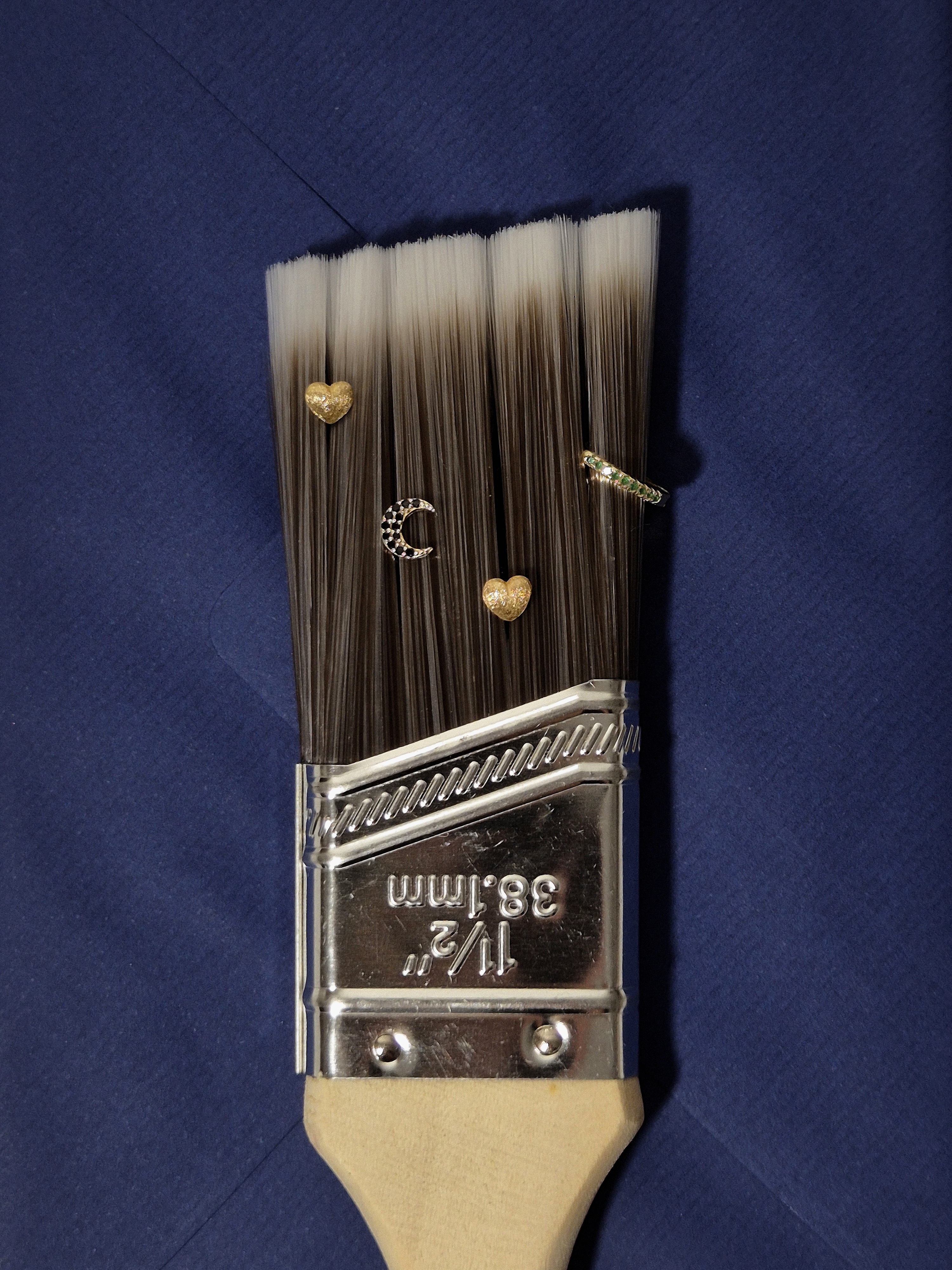 Paintbrush still life with gold earrings arranged on the bristles, placed over a blue paper envelope.