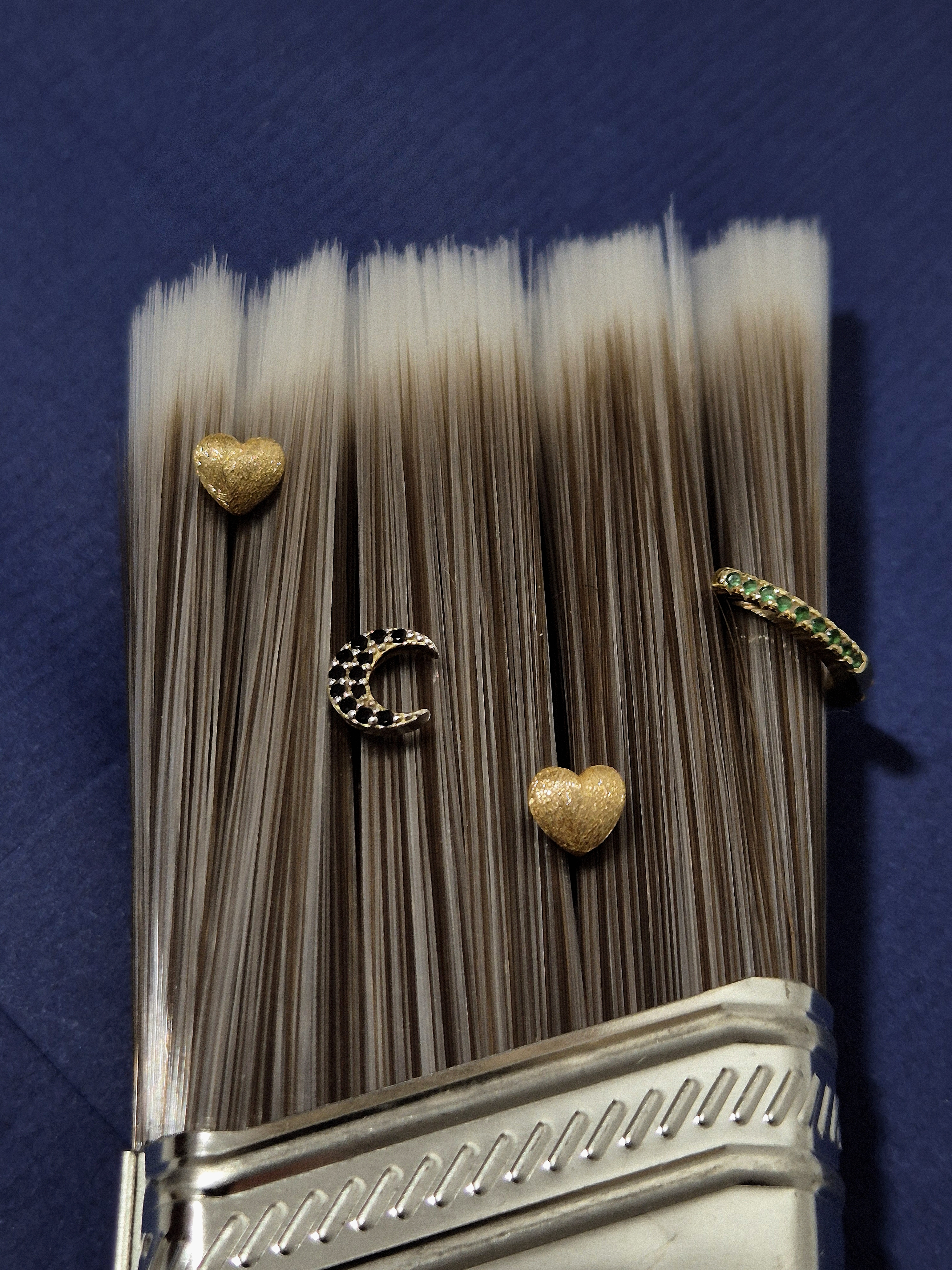 Close-up of gold earrings arranged on the bristles of a paintbrush over a blue paper envelope.