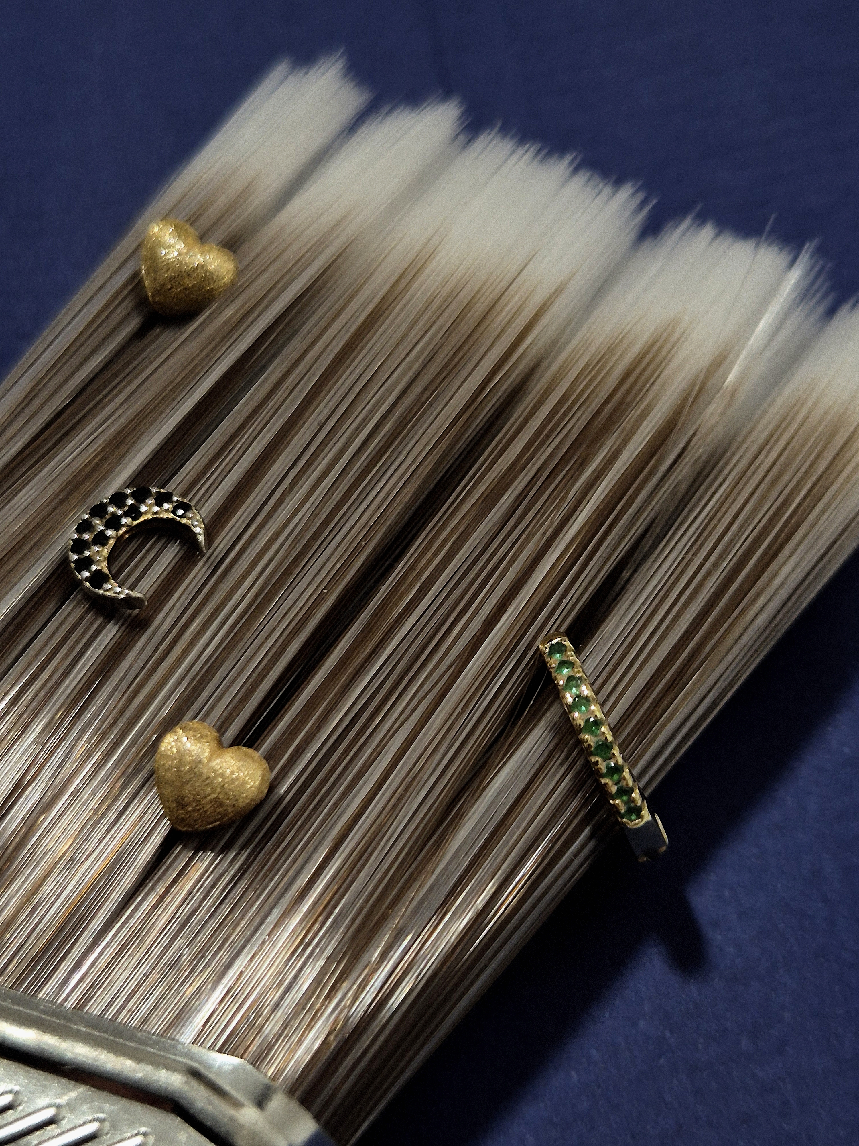 Detailed close-up of a paintbrush with gold earrings placed on its bristles.