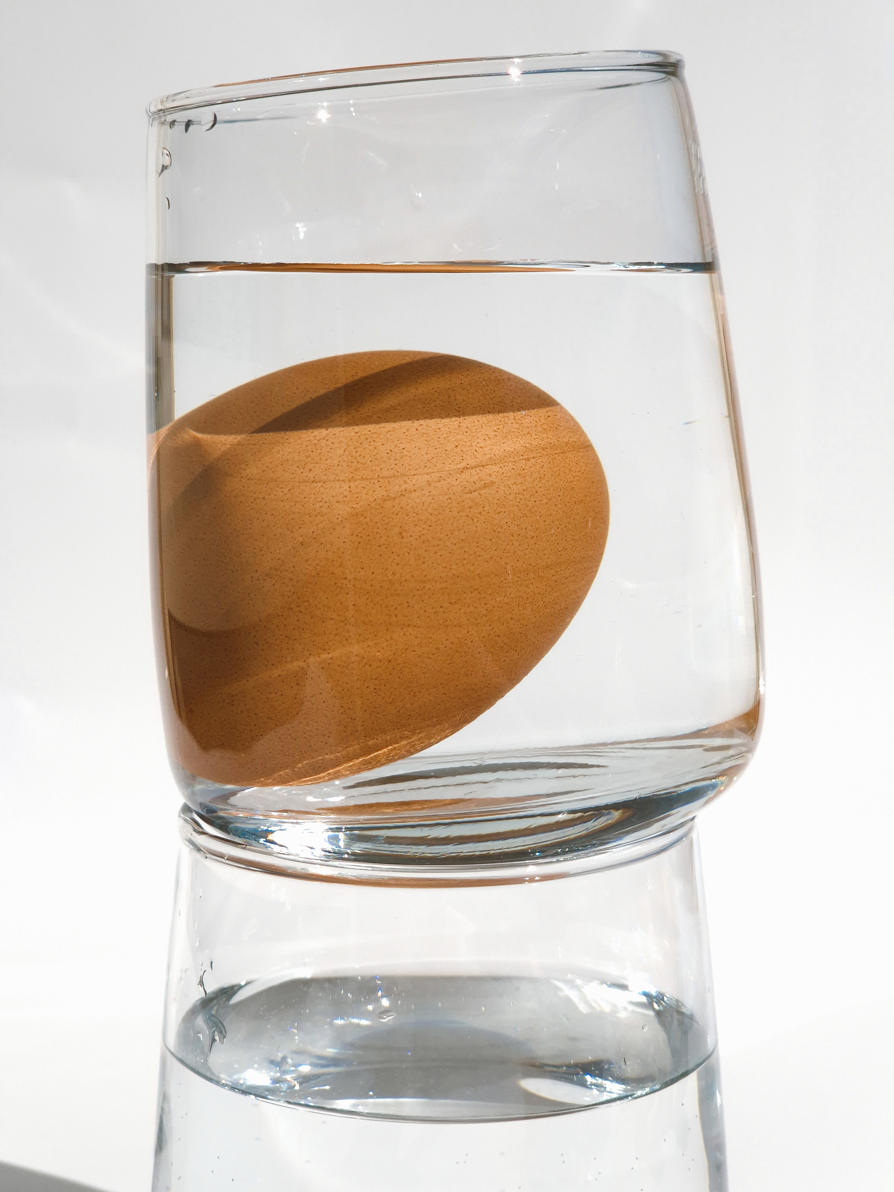 Egg floating in a glass filled with water, stacked on top of another glass.