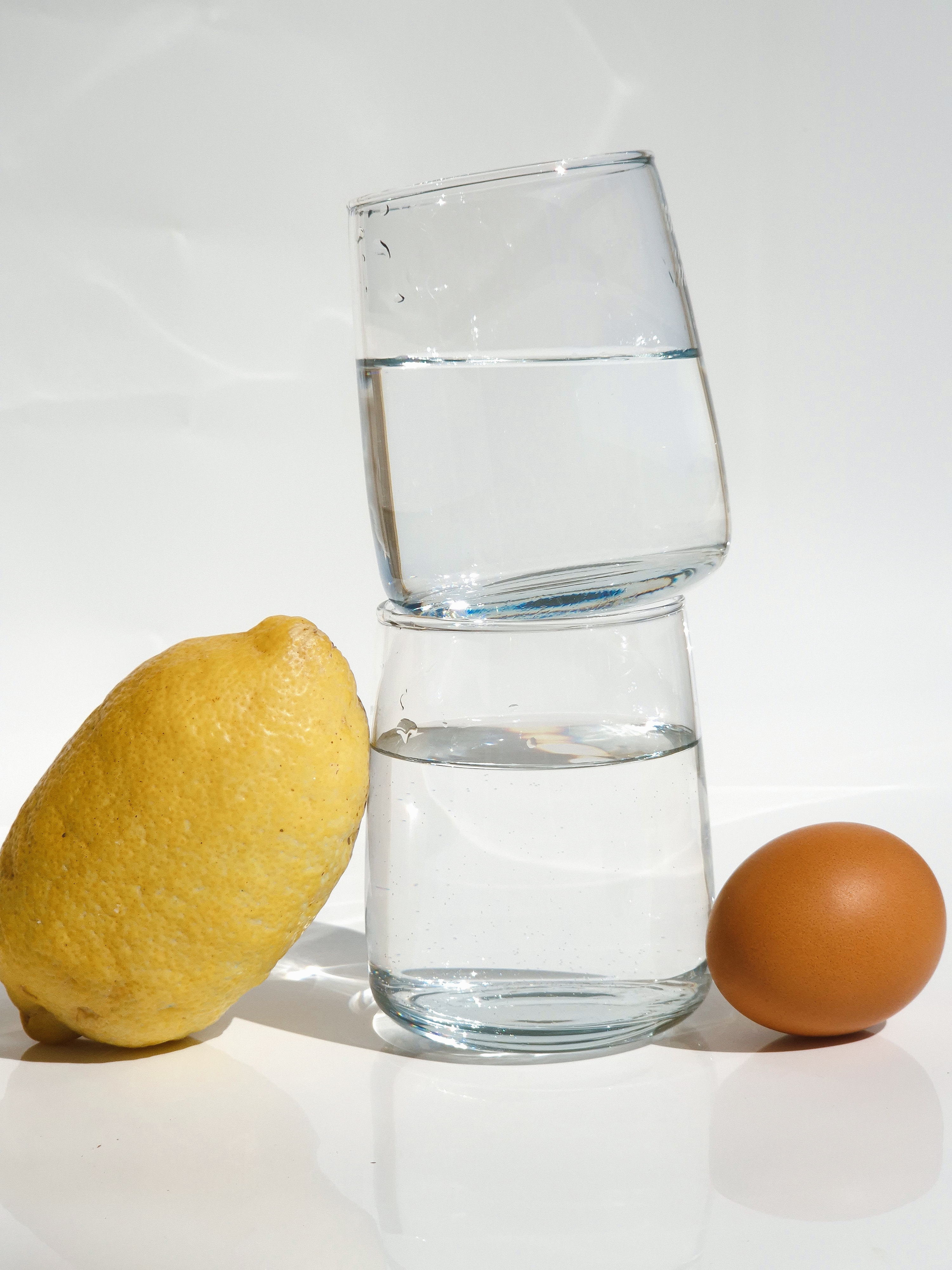 Still life with a lemon, an egg and two stacked glasses filled with water.