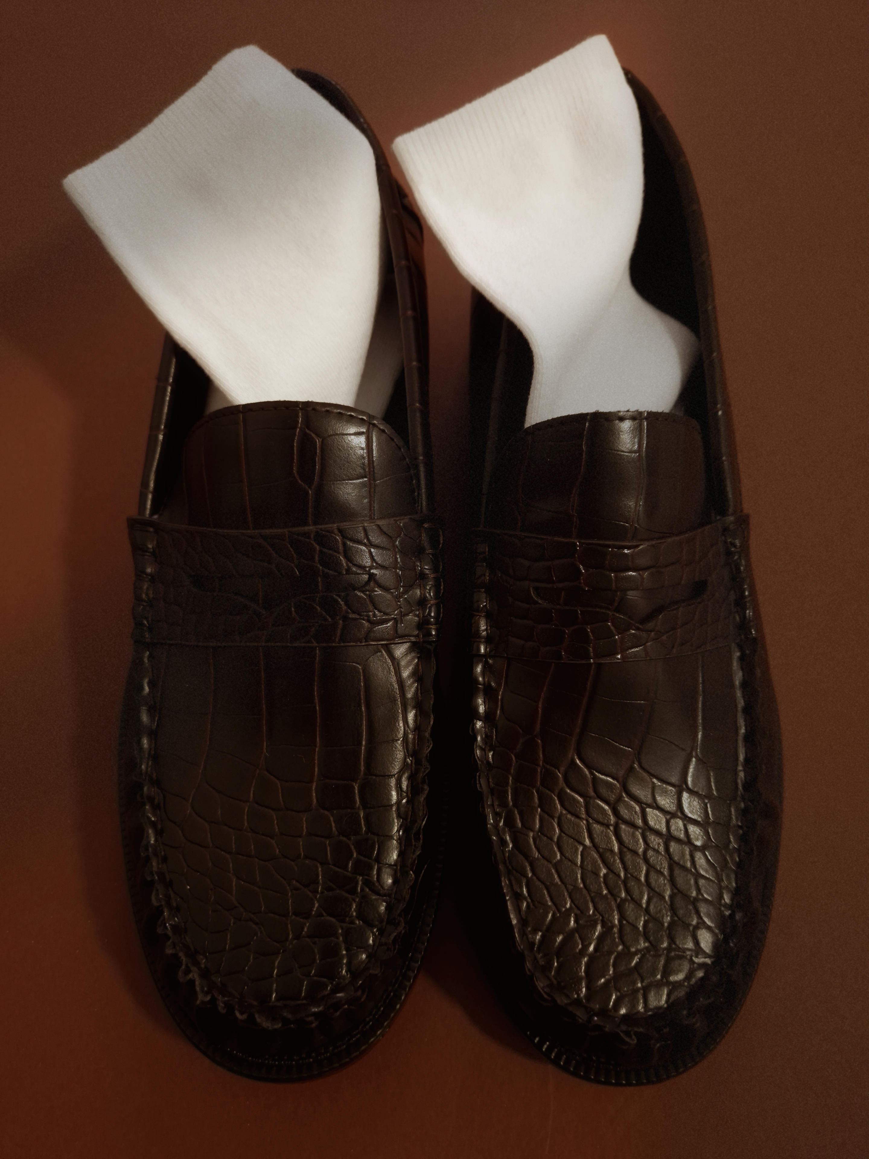 Brown leather loafers filled with white socks, photographed from above on a warm brown background.