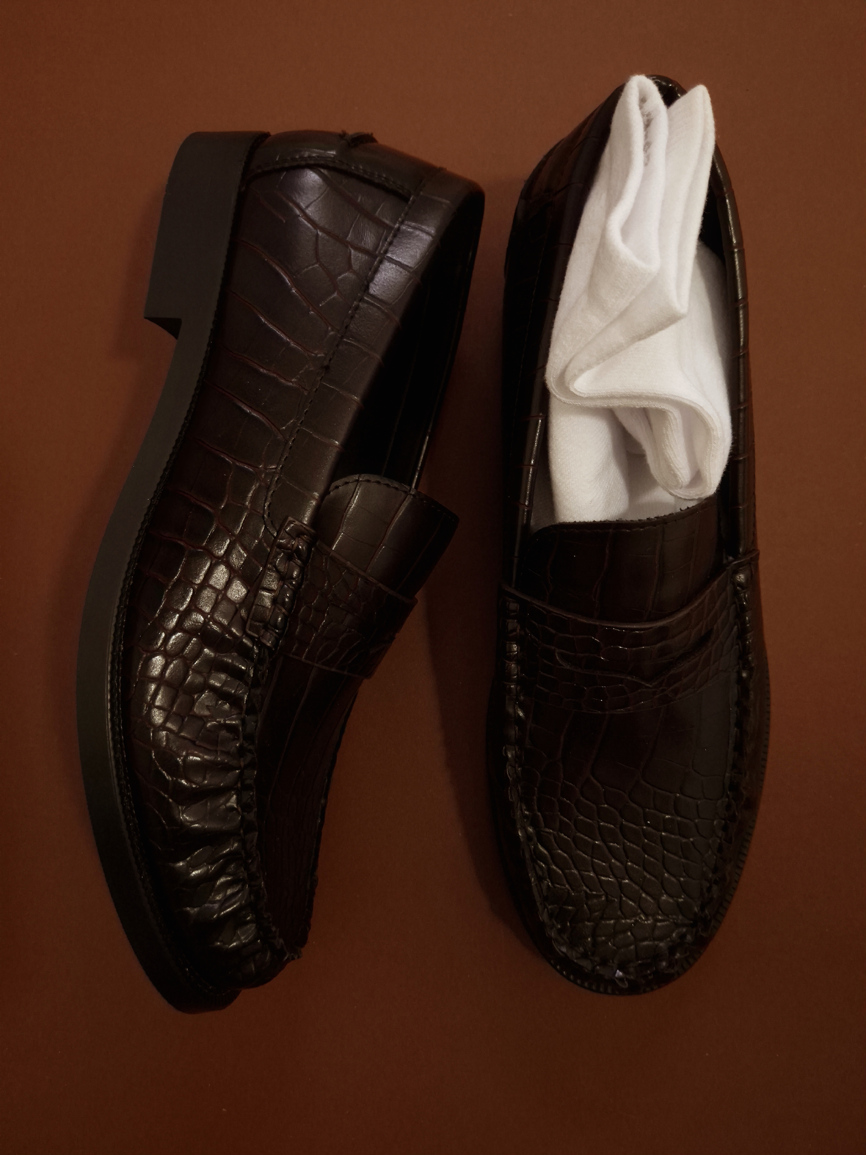 Two brown leather loafers on a brown surface, one standing upright and one filled with folded white socks.