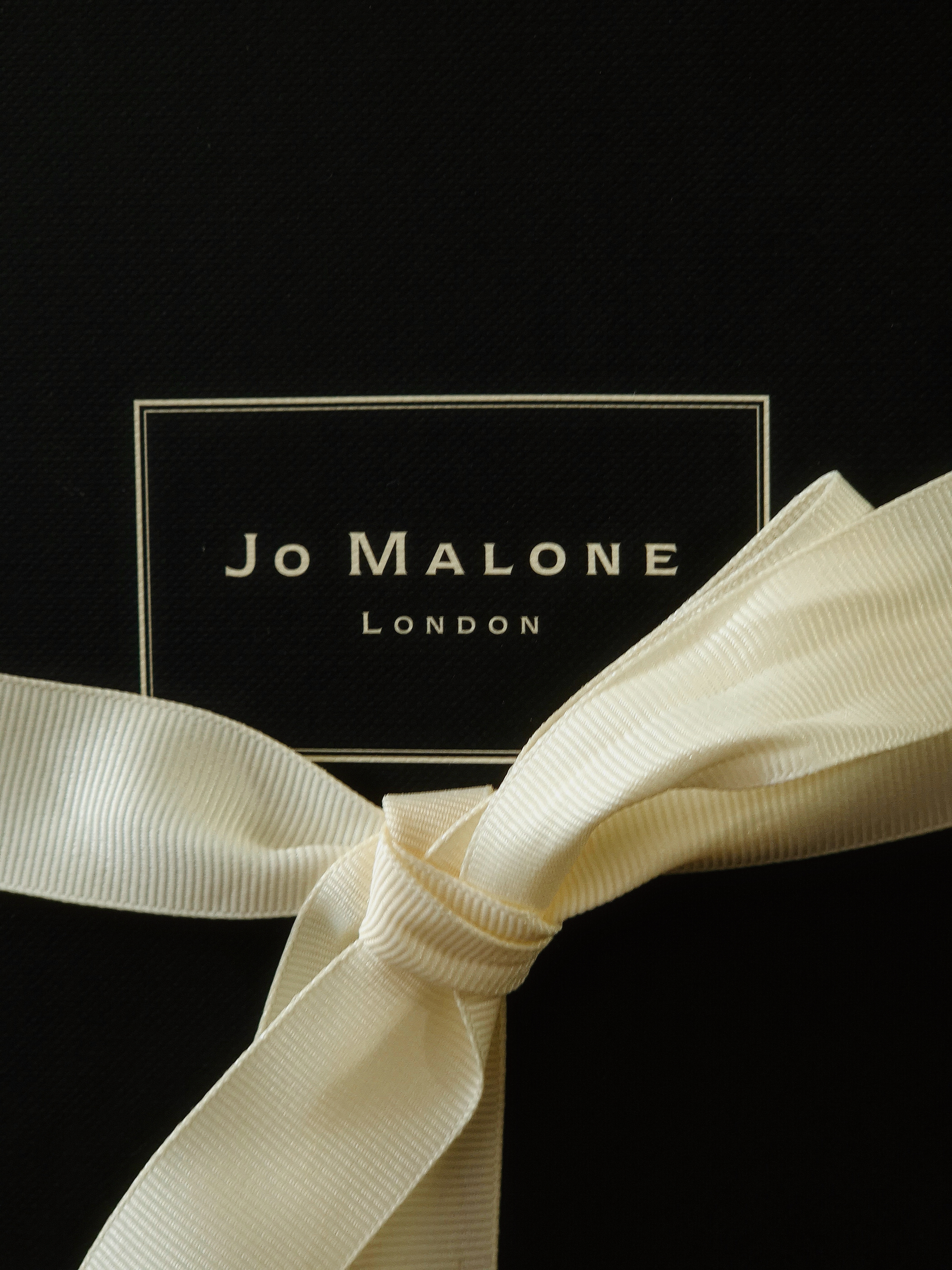 Detail of a cream and black Jo Malone fragrance box with ribbon.