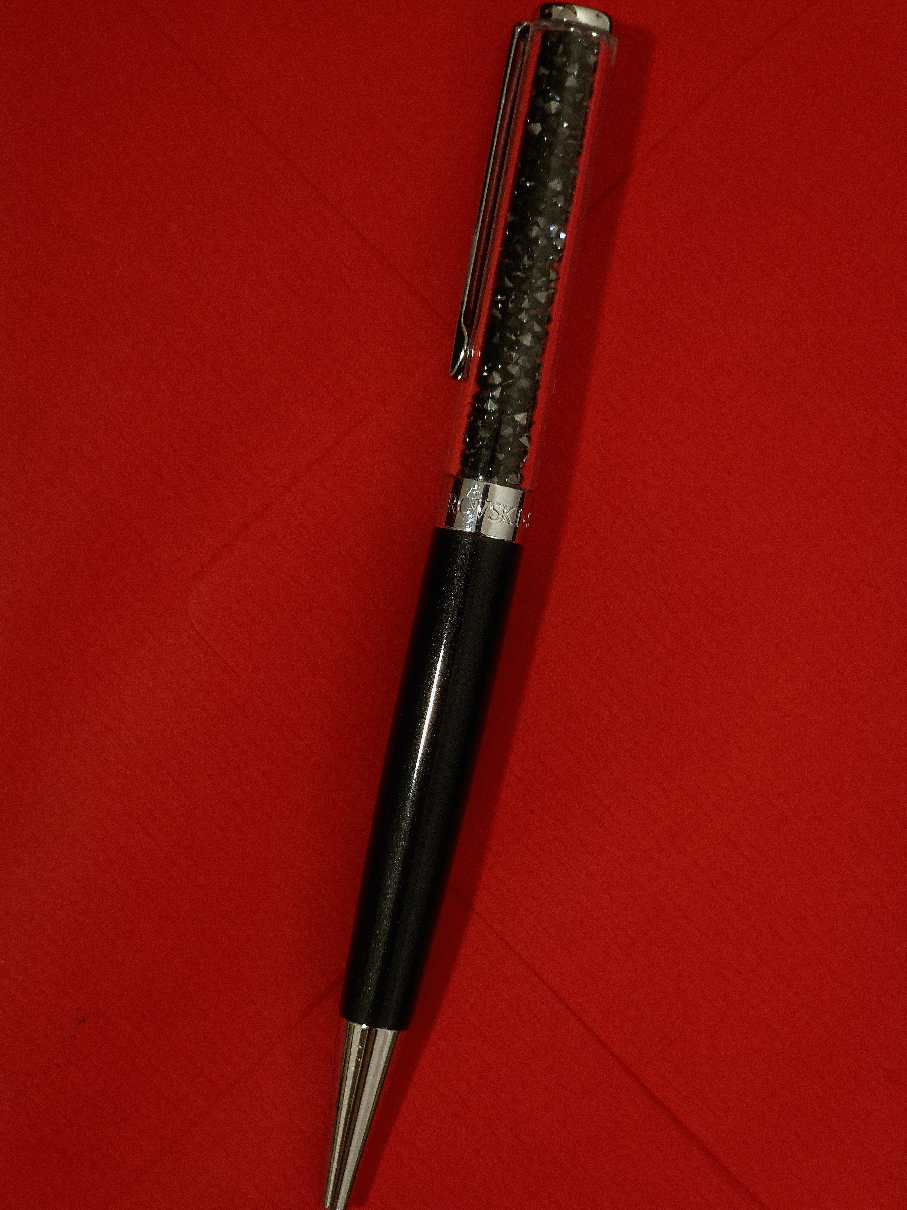 Close-up of a black writing instrument resting diagonally on a red envelope against a dark textured surface.