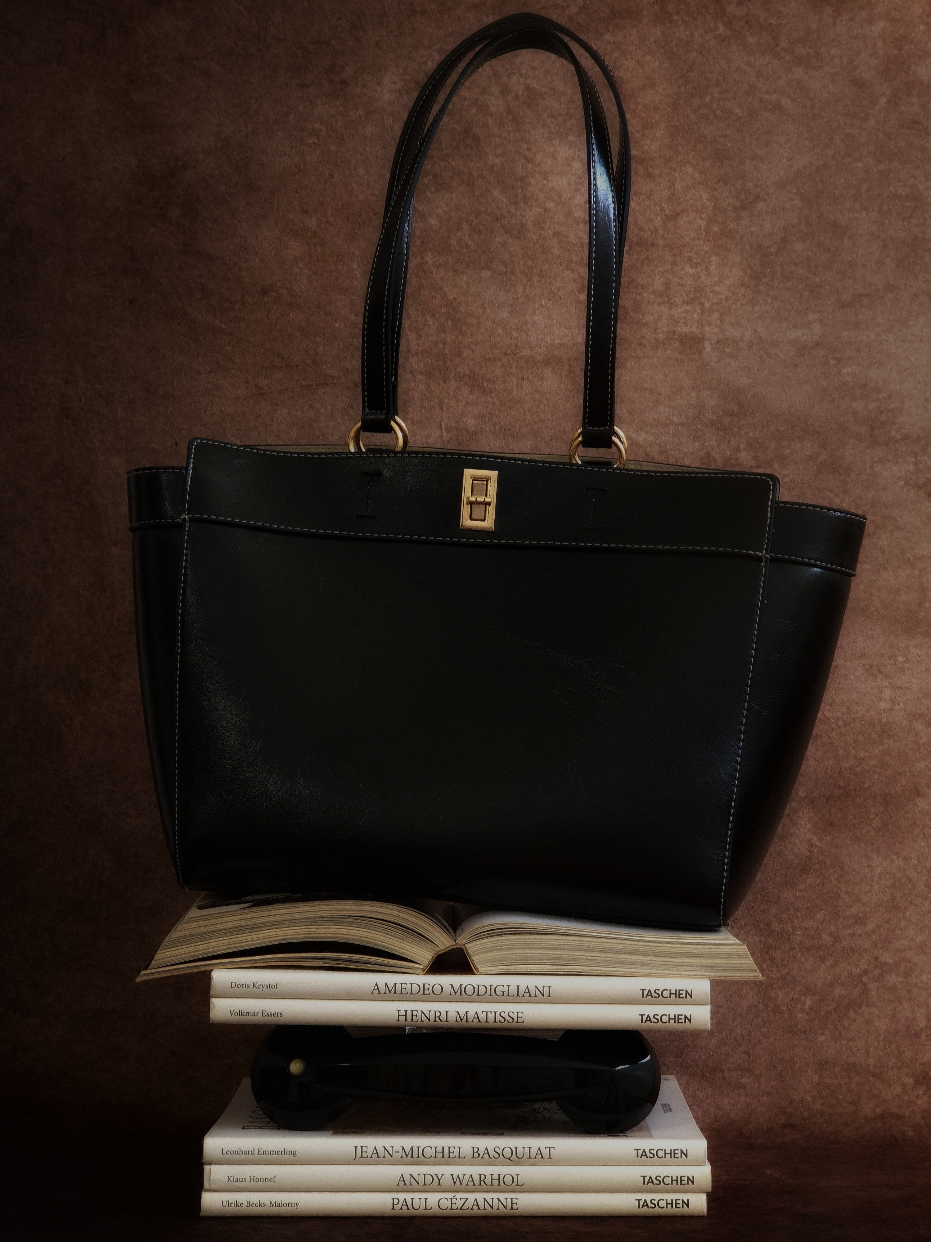 Black handbag displayed on a stack of books in a minimalist still life composition.