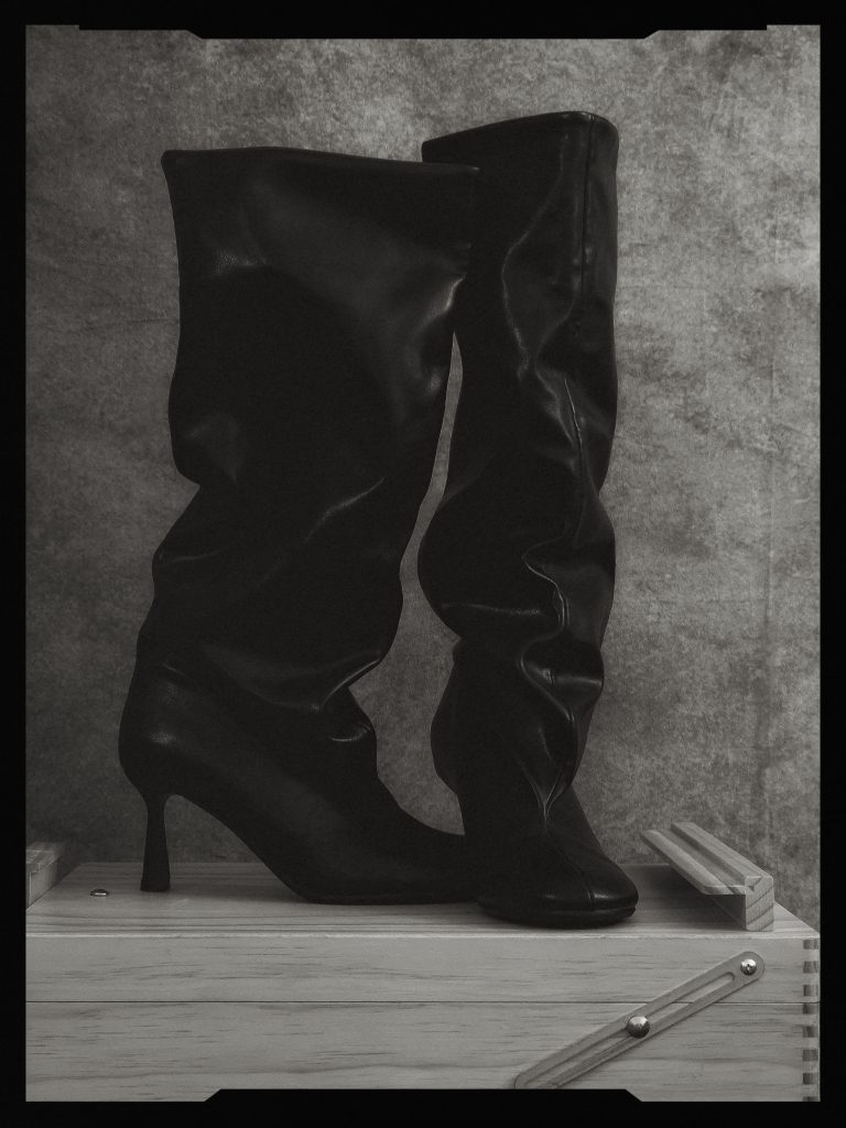 Black-and-white still life of tall black boots photographed against a dark background.