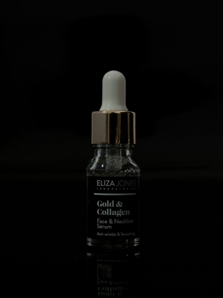 Glass dropper bottle of gold-infused serum against a black background.