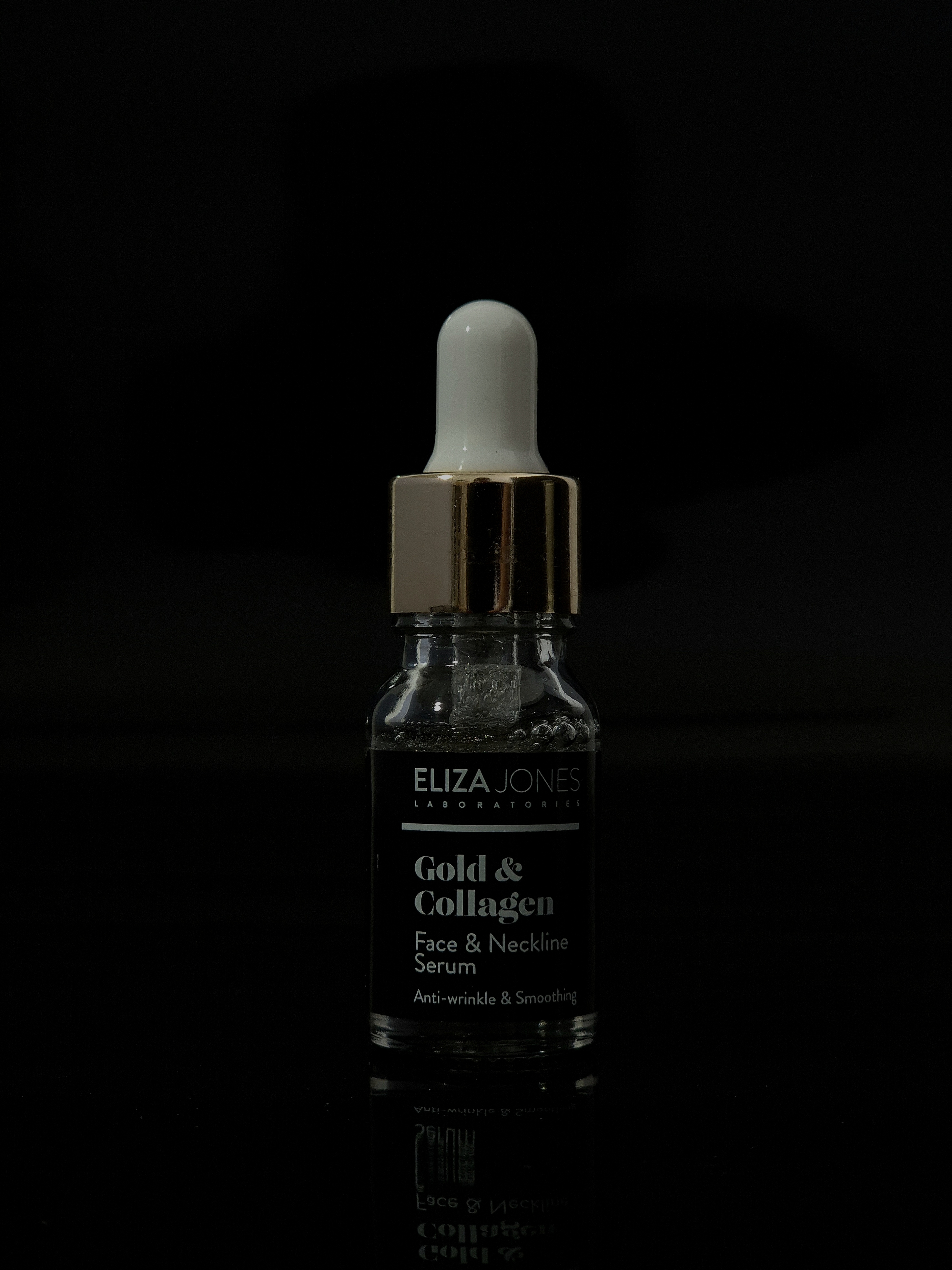Glass dropper bottle of gold-infused serum against a black background.