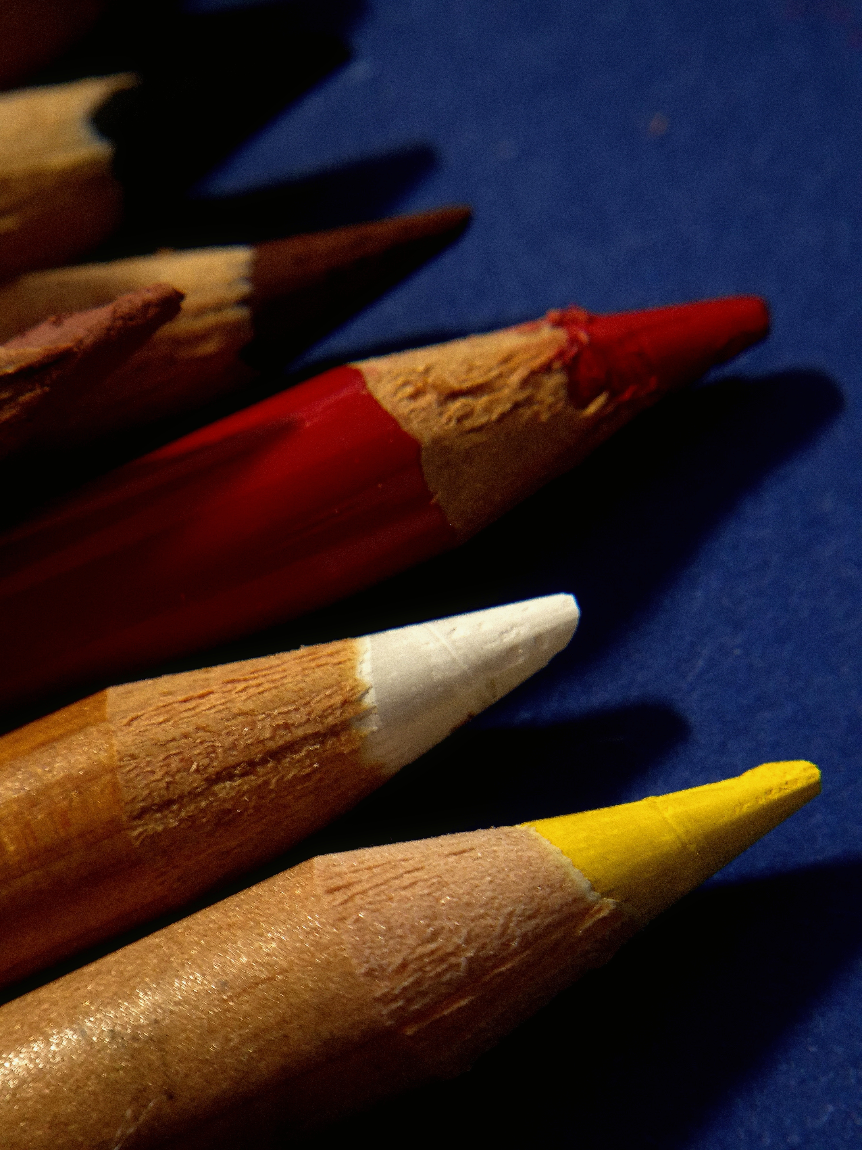 Close-up of red, white, and yellow pencil tips on a blue surface.